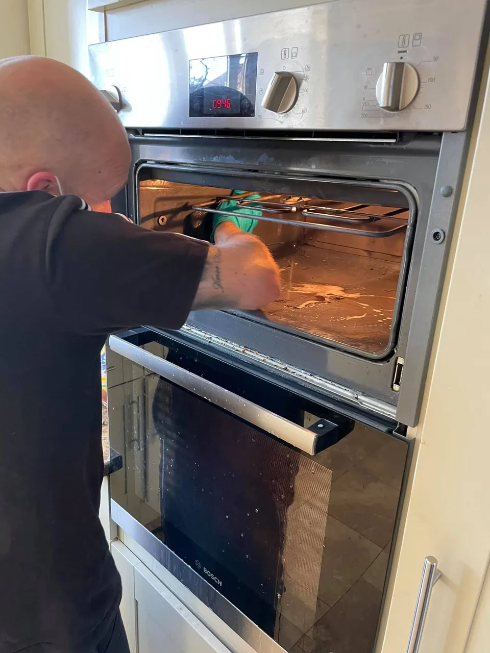 A trainee in gloves cleaning the inside of a built-in oven during a job