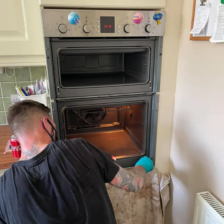 A trainee cleaning a double oven on a real job in a kitchen